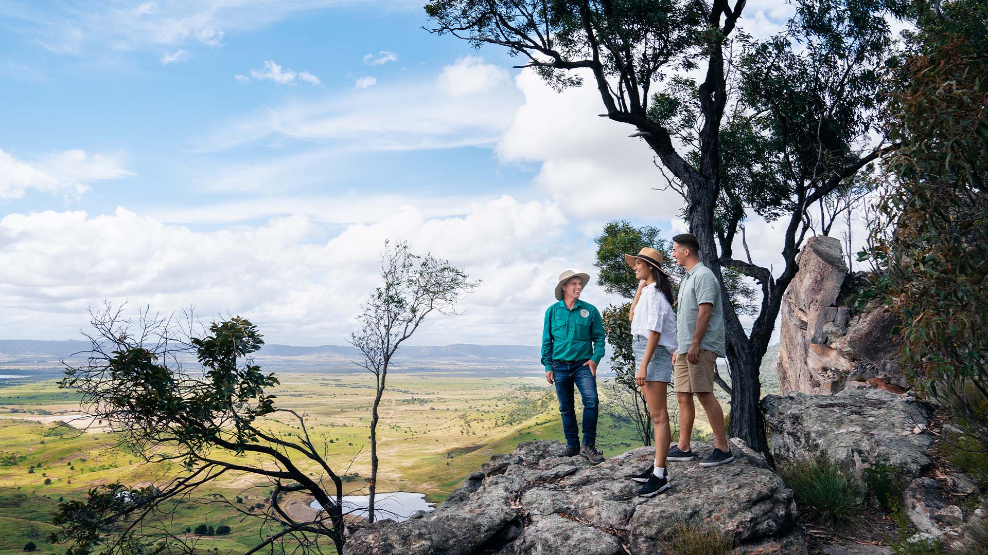 Three people standing on a rock edge looking over Arcadia Valley, Queensland